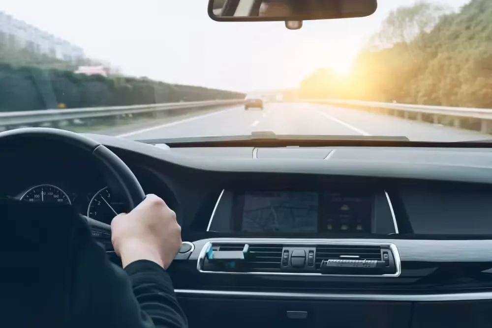 Mão no volante de um carro em uma estrada ao pôr do sol